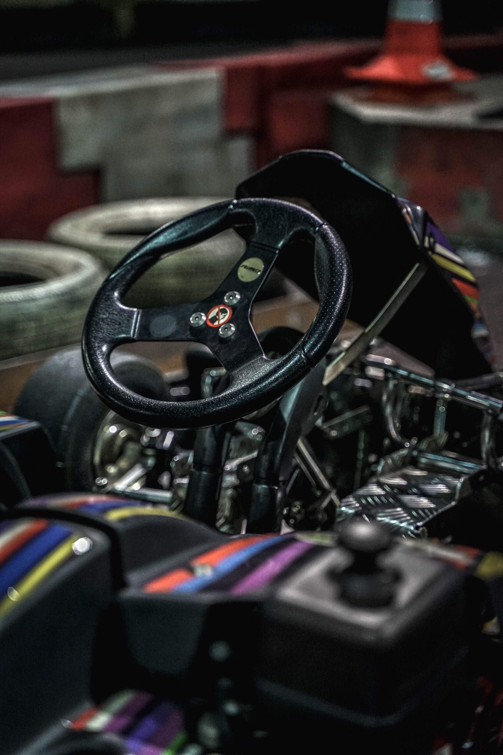 Detailed view of a go-kart steering wheel on an indoor racing track with tires in the background.